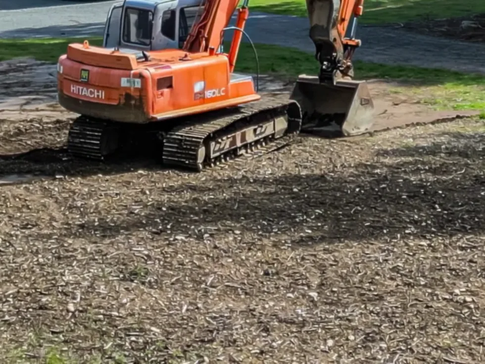 A tracked excavator working on open ground strewn with wood chips from clearing