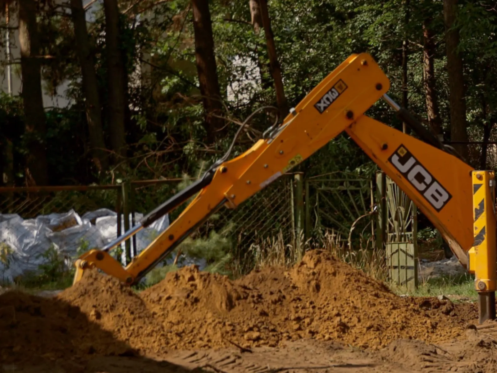 The boom and stabiliser of a backhoe loader beside a pile of freshly dug sandy soil